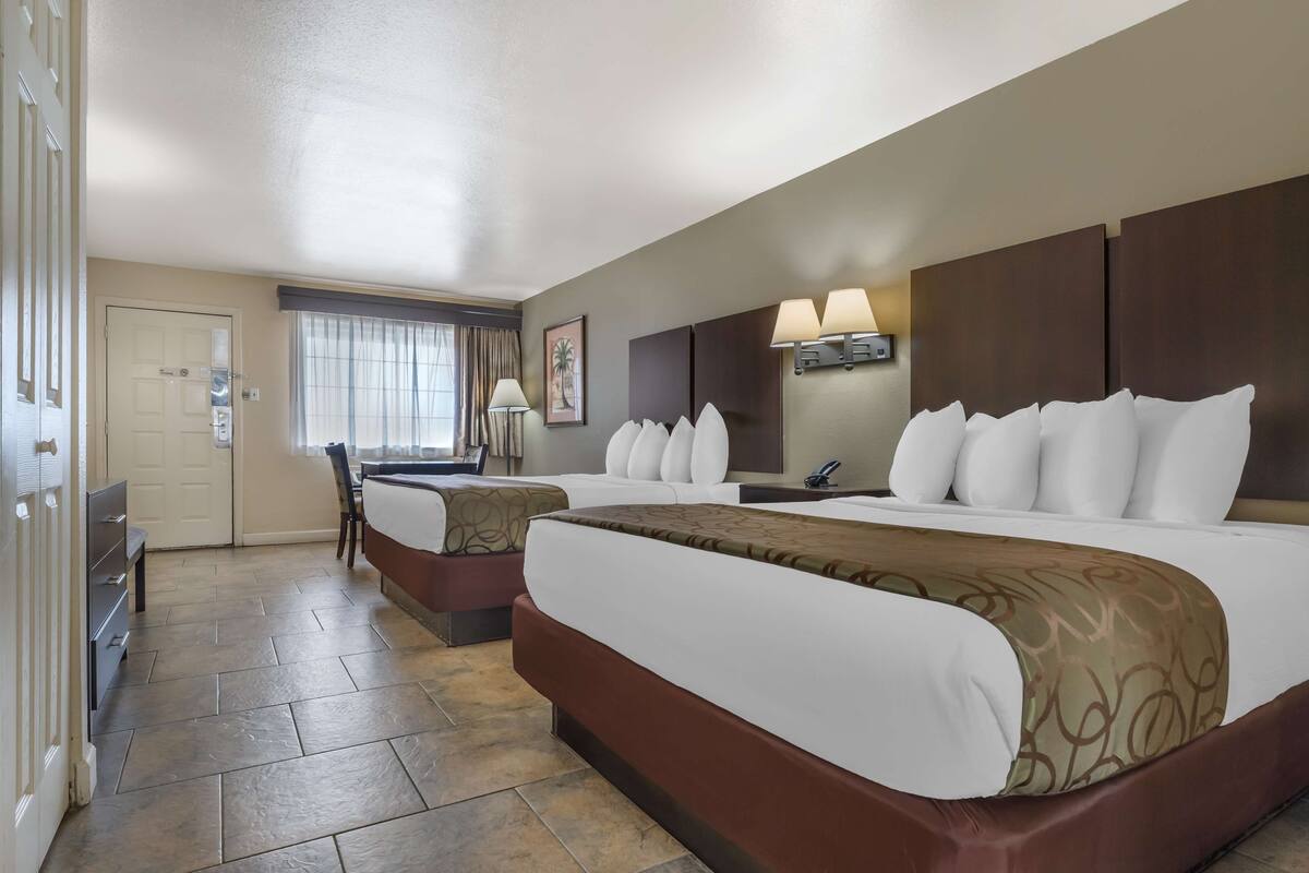 A hotel room with two beds, a desk, a chair, and a window with curtains.