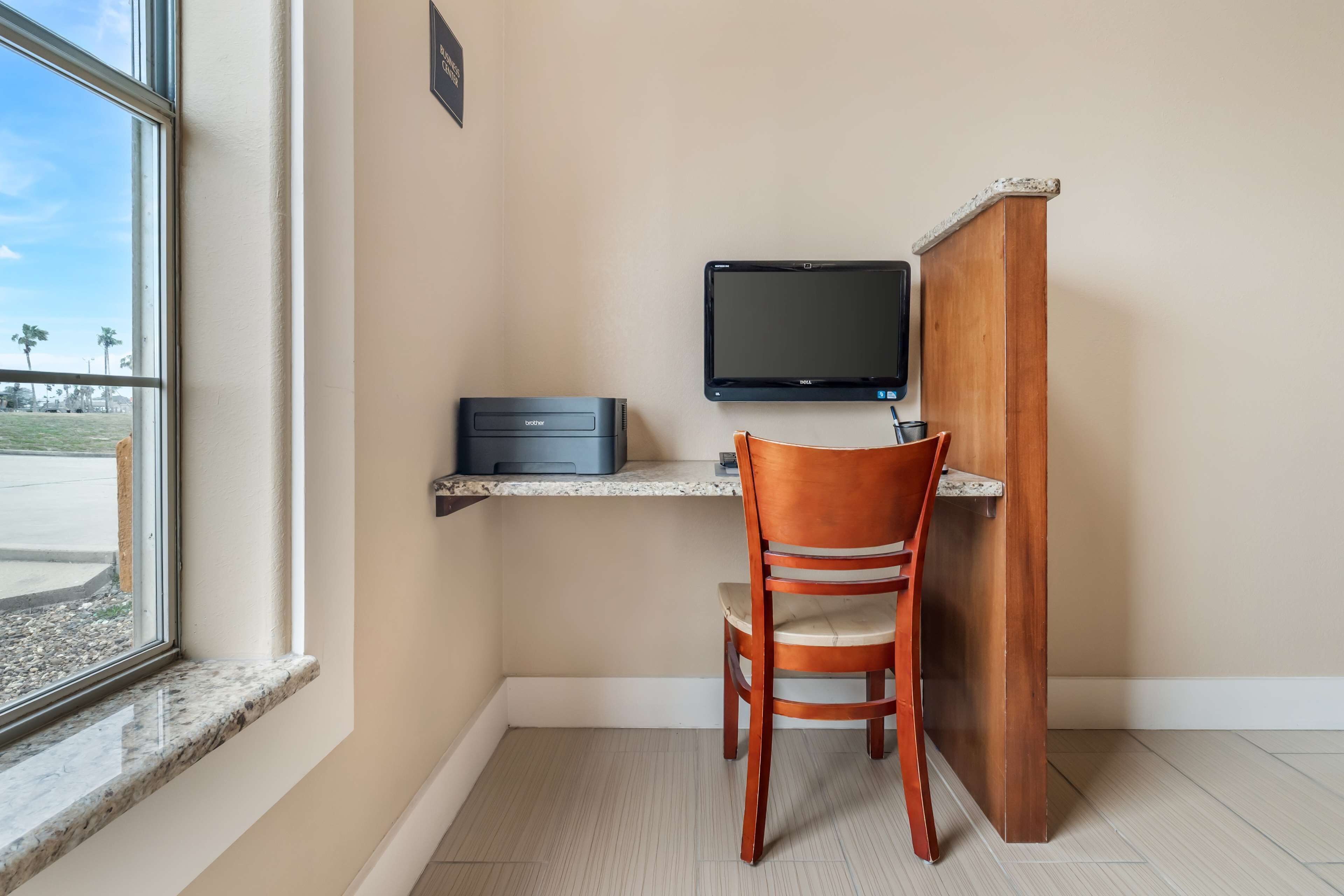A small office space with a desk, chair, computer, printer, and a window with a view of palm trees.