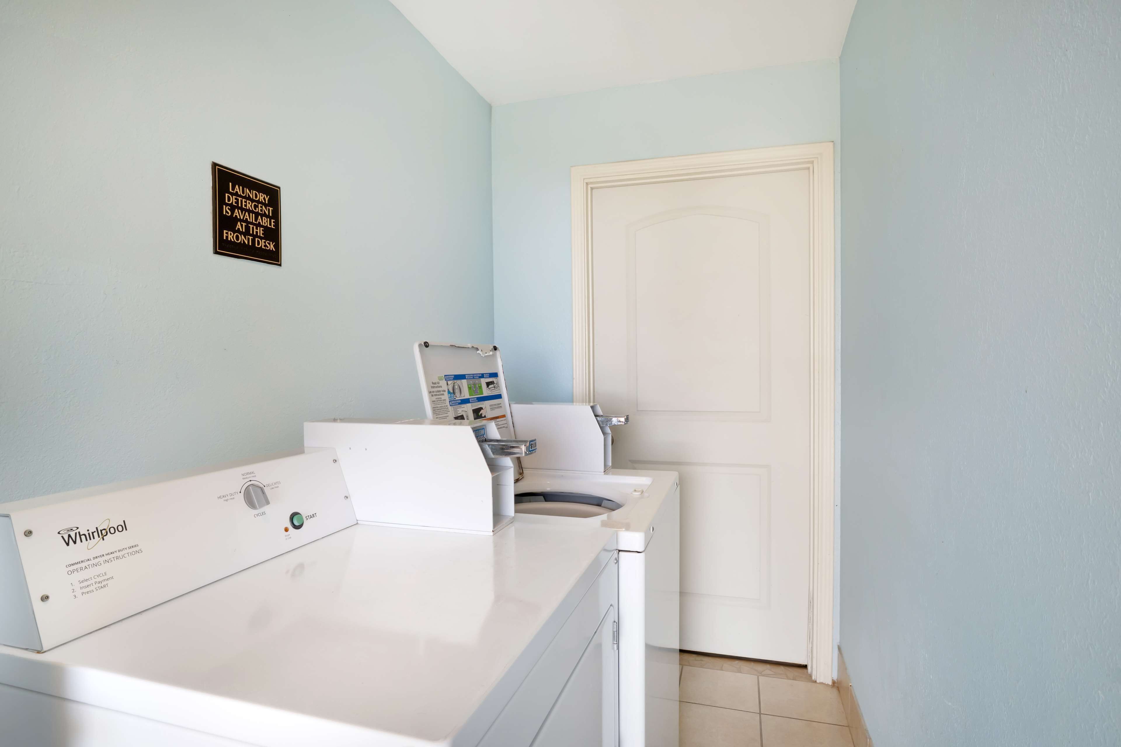 A laundry area with a Whirlpool washer and dryer, a sign indicating detergent availability at the front desk, and a white door.