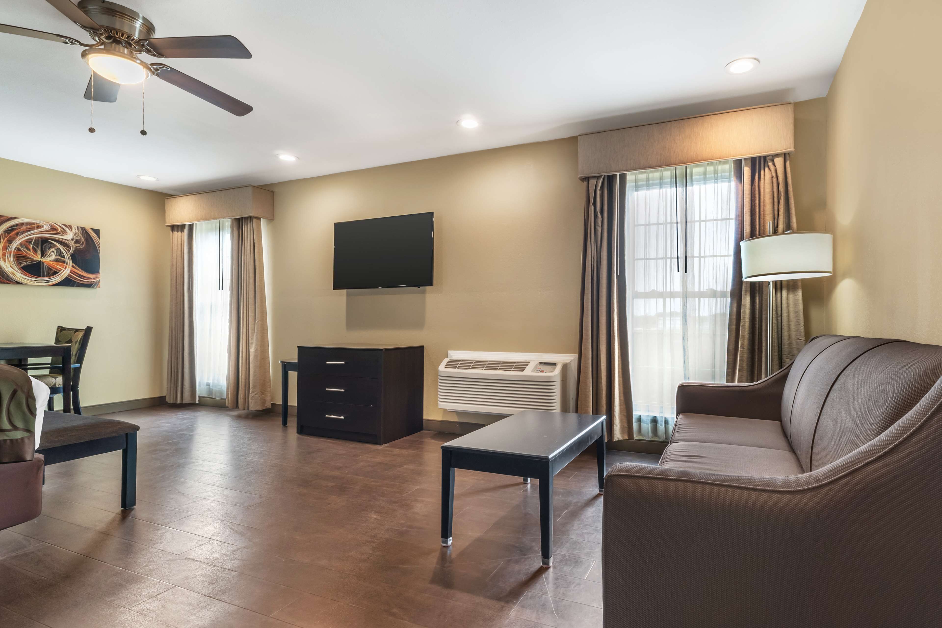 A modern living room with a flat-screen TV, a ceiling fan, a sofa, a coffee table, and a dining area with chairs.