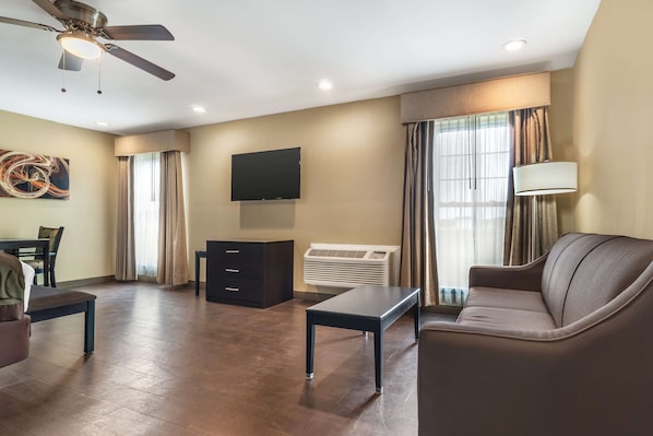 A modern living room with a flat-screen TV, a ceiling fan, a sofa, a coffee table, and a dining area with chairs. - Best Western Padre Island (Corpus Christi)
