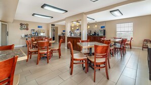 A spacious dining area with multiple wooden tables and chairs, a kitchen area with cabinets and appliances, and a bar counter.