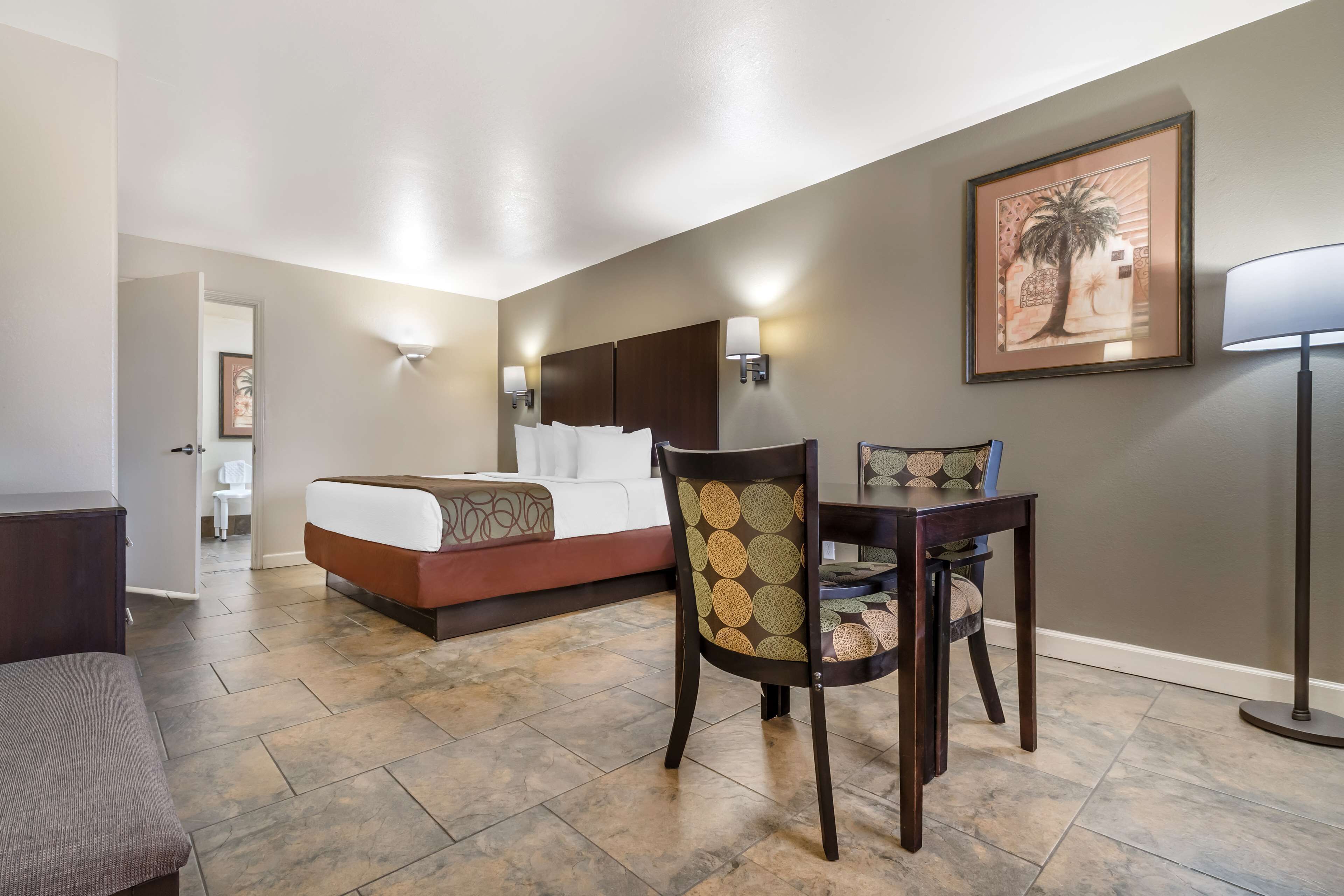 A hotel room with a bed, a desk, a chair, and a lamp.