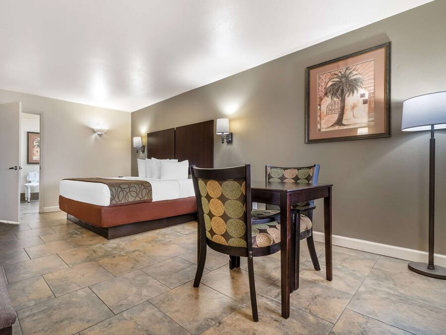 A hotel room with a bed, a desk, a chair, and a lamp.