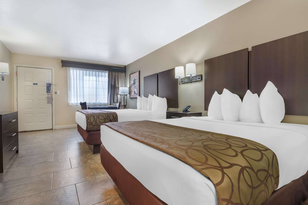 A hotel room with two beds, a desk, a chair, a wardrobe, and a window with curtains.