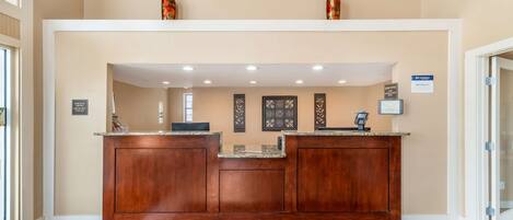 A reception area with a wooden reception desk, a black doormat, and framed artwork on the wall.