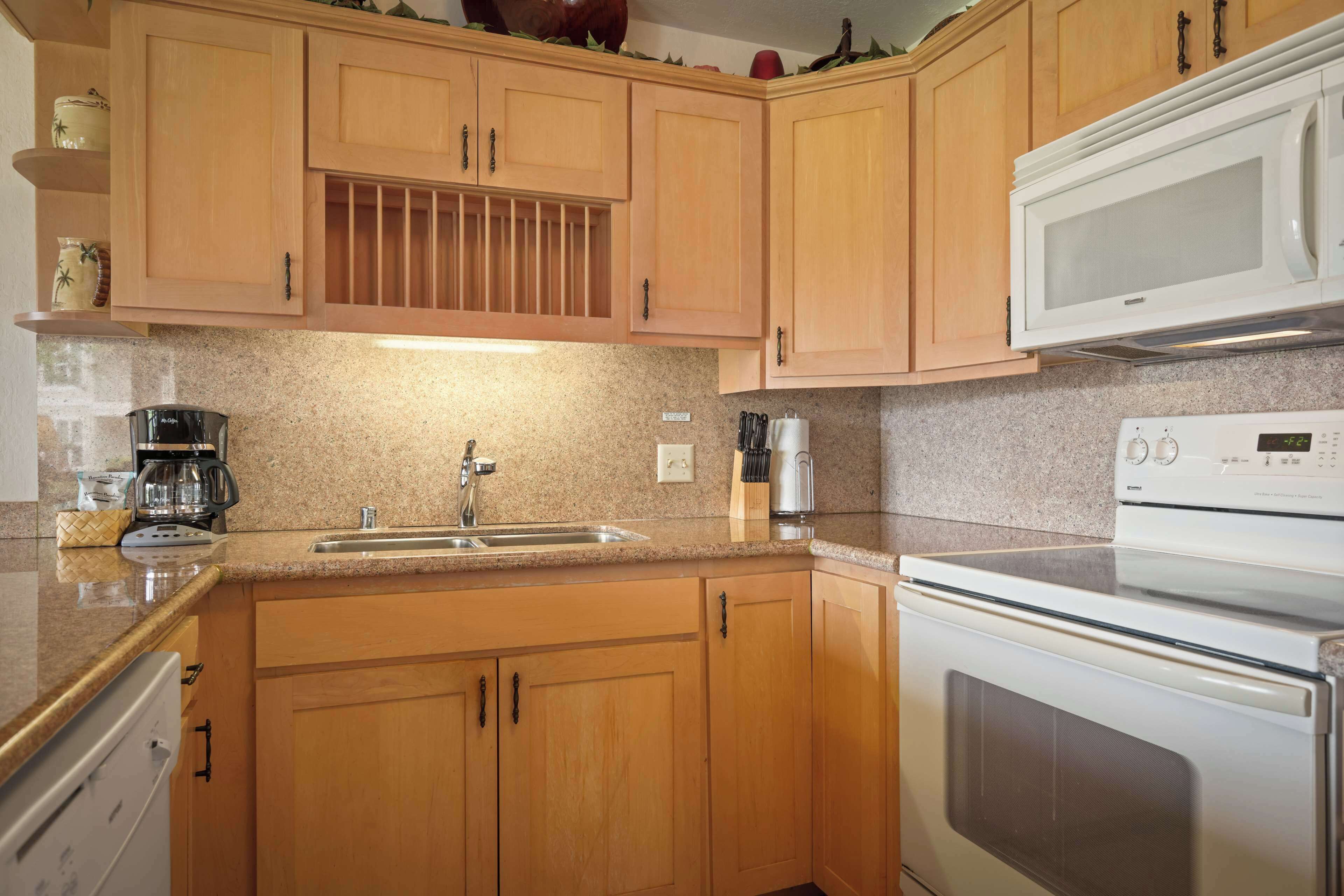 A kitchen with wooden cabinets, a stainless steel sink, a white microwave, and a built-in oven.