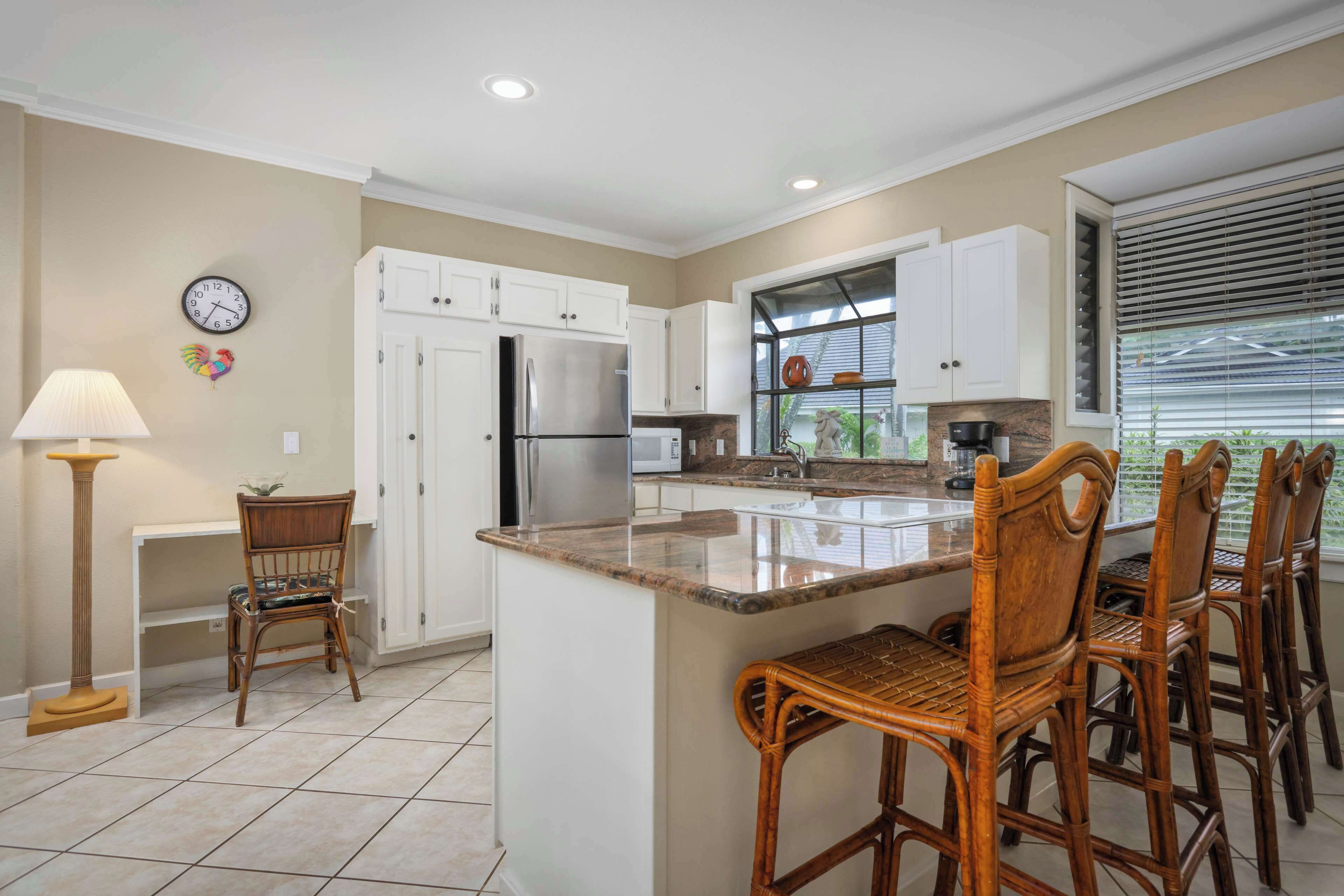 A modern kitchen with white cabinets, a stainless steel refrigerator, a built-in oven, and a large island with bar stools.