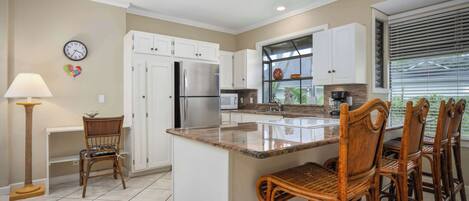 A modern kitchen with white cabinets, a stainless steel refrigerator, a built-in oven, and a large island with bar stools.