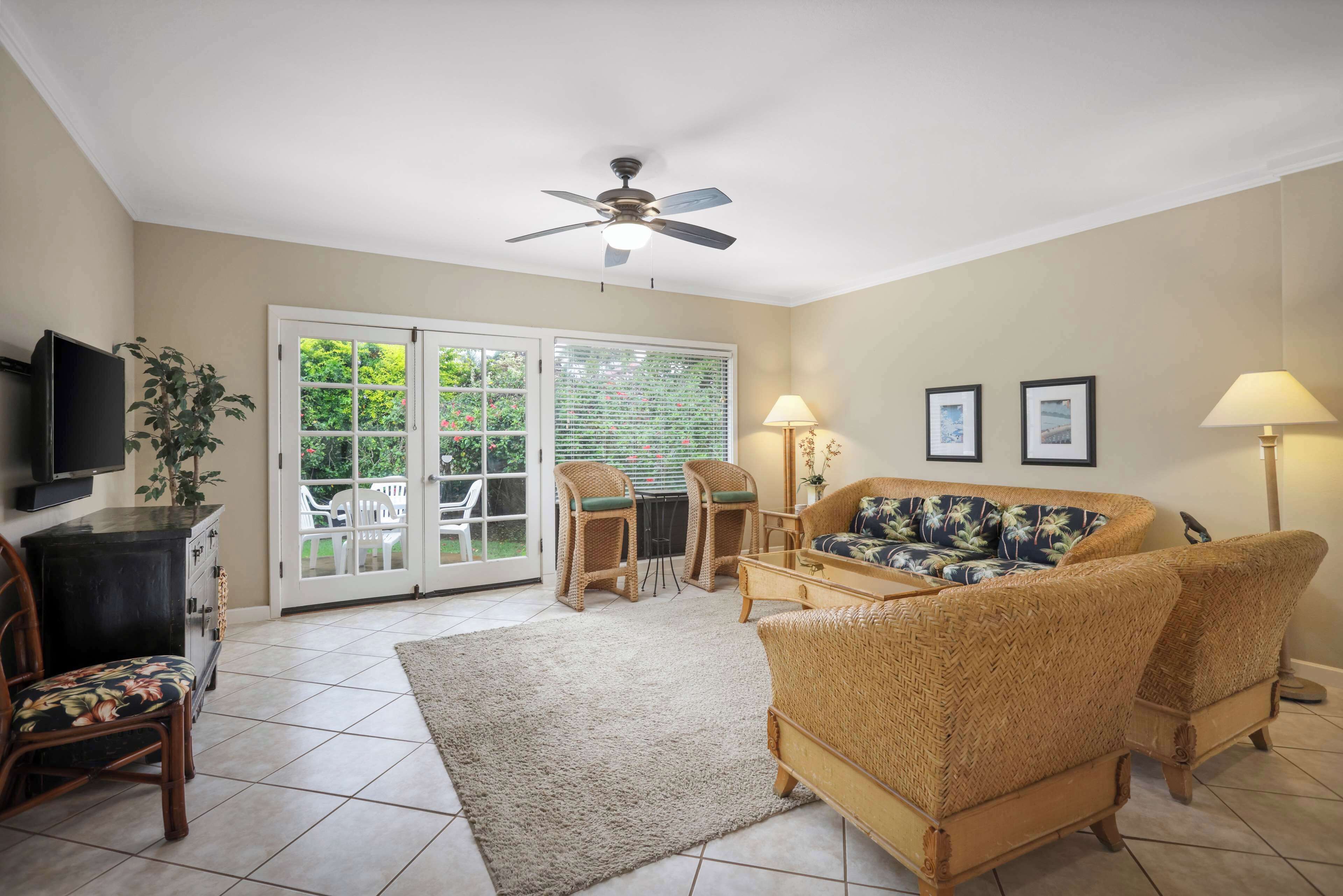 A living room with a ceiling fan, a sofa, two chairs, a coffee table, a TV, and a plant.