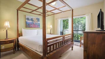 A four-poster bed with a wooden frame, two bedside tables with lamps, a painting on the wall, a television on a wooden cabinet, and a balcony with a view of greenery.