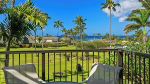 A balcony with a table and chairs, overlooking a lawn with palm trees and a view of the ocean. - Aston at Poipu Kai (Koloa)