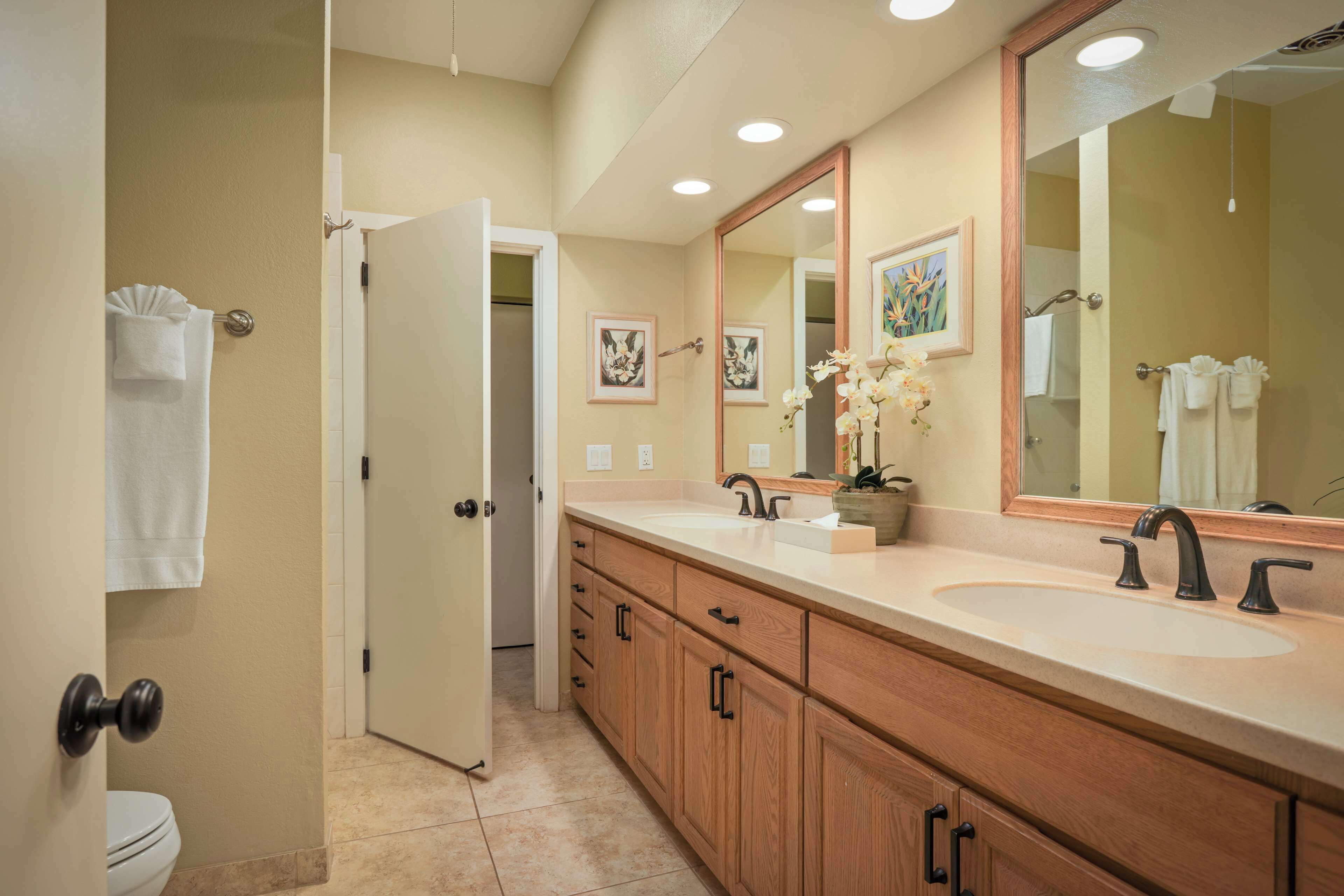 Un baño con lavamanos doble, armarios de madera, un espejo grande y una puerta que da a otra habitación.