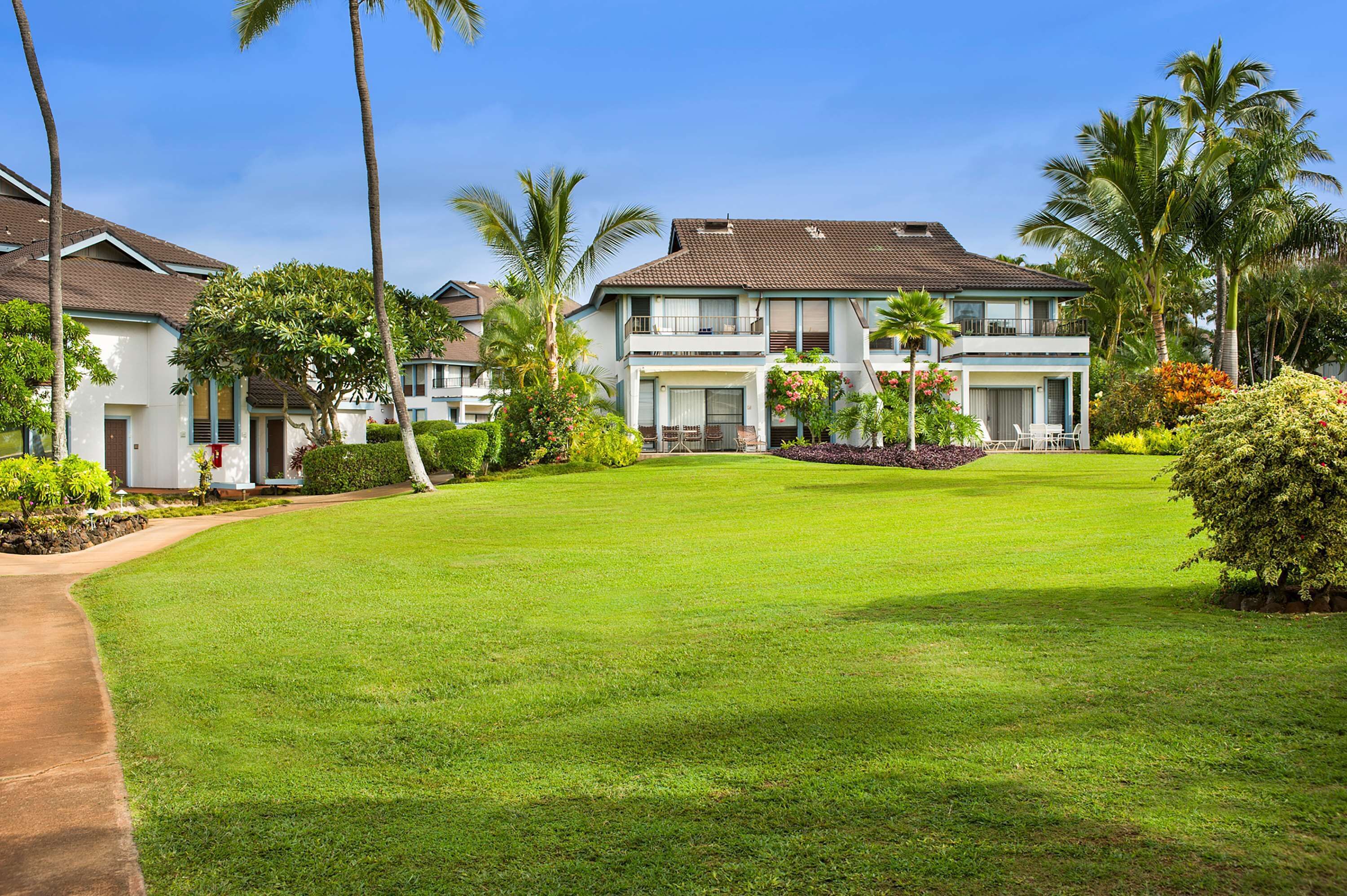 A two-story building with a flat roof, surrounded by a well-maintained lawn and palm trees.