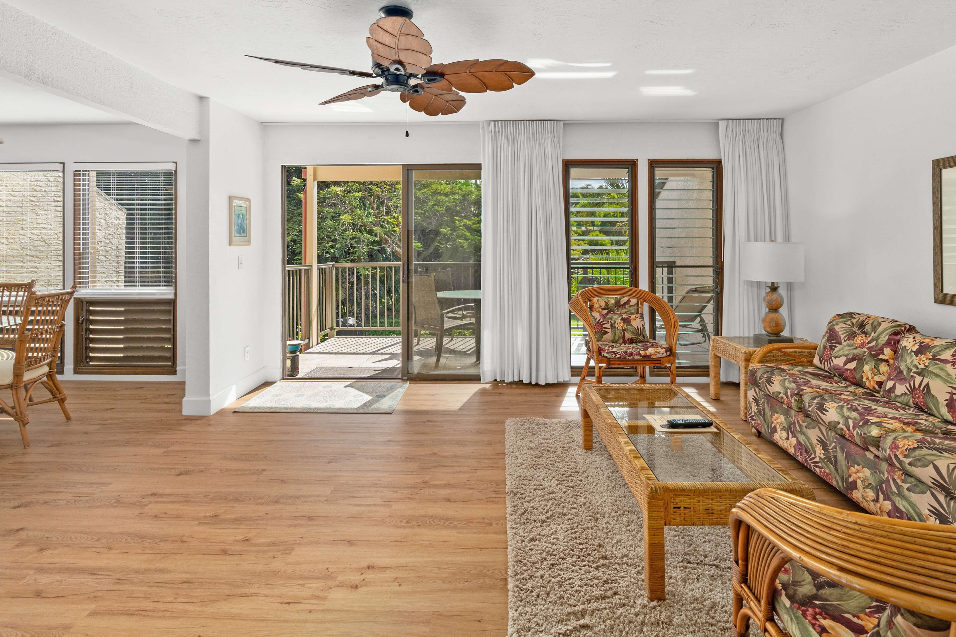 Un salon spacieux doté d’un plancher en bois, d’un ventilateur de plafond, d’un canapé, d’une table basse et d’un coin repas avec des chaises.
