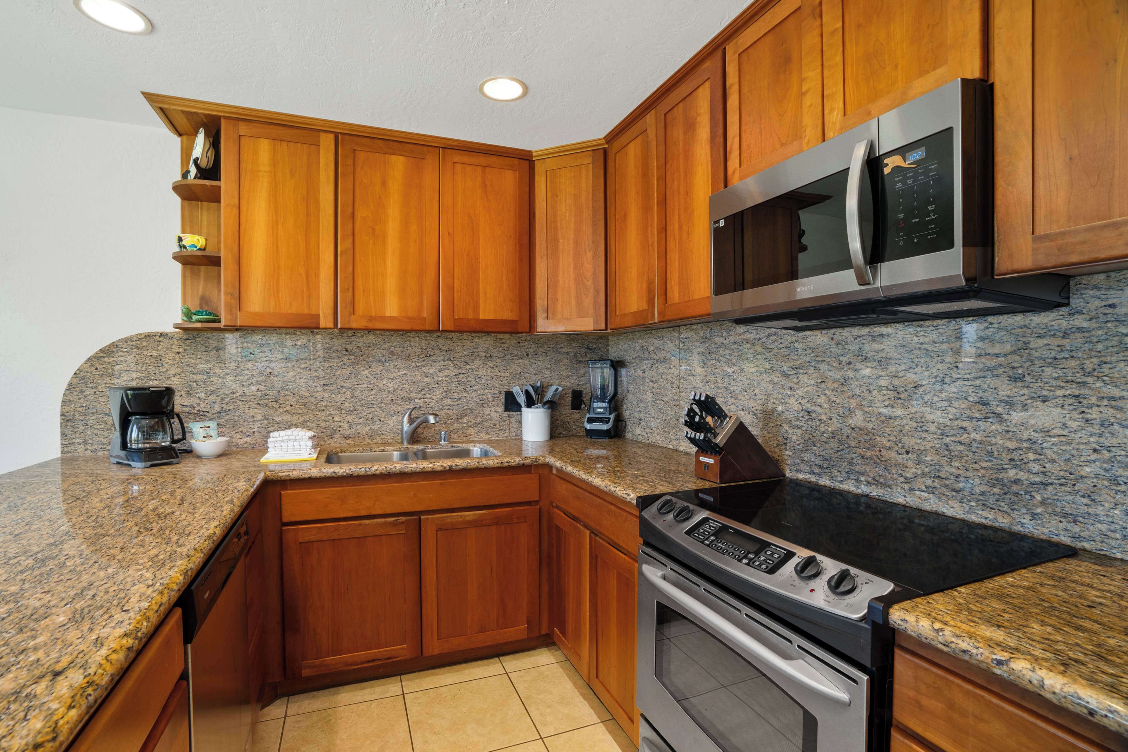 Una cocina con gabinetes de madera, encimeras de granito, microondas de acero inoxidable, estufa y cafetera.