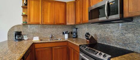 Una cocina con gabinetes de madera, encimeras de granito, microondas de acero inoxidable, estufa y cafetera.