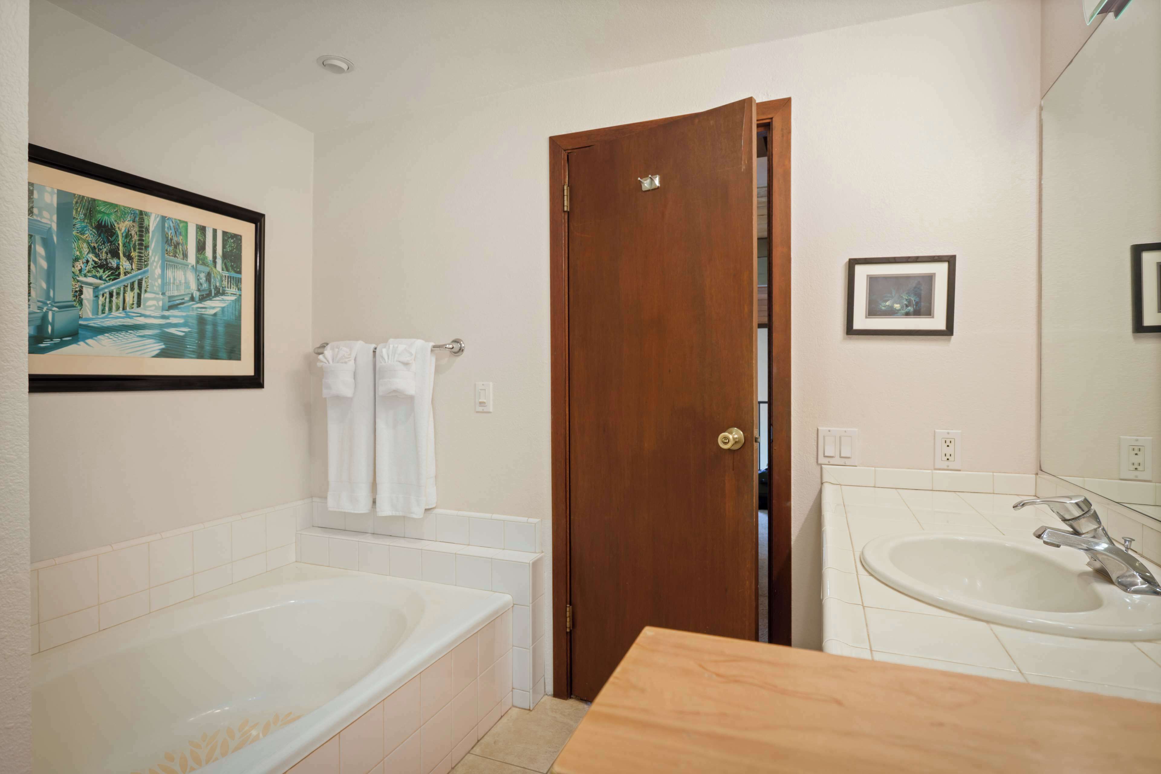 Un baño con bañera, una puerta de madera, un lavamanos y un cuadro enmarcado en la pared.