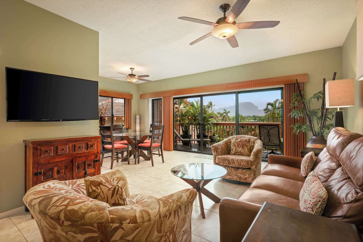 A spacious living area with a flat-screen TV, leather sofas, a glass coffee table, and ceiling fans.