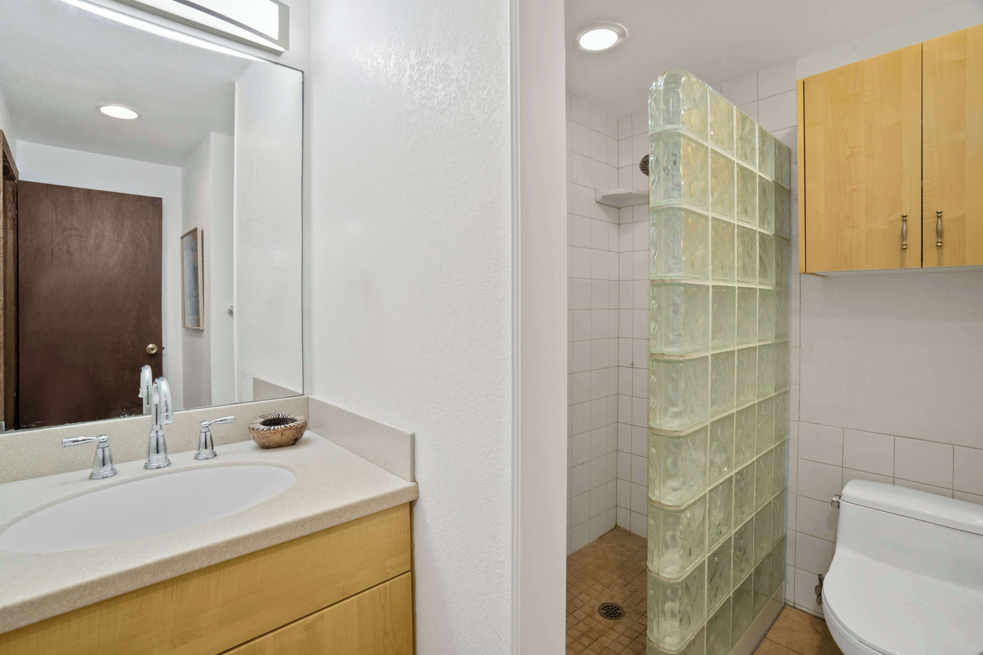 A bathroom with a white sink, wooden cabinets, a glass shower enclosure, and a white toilet.