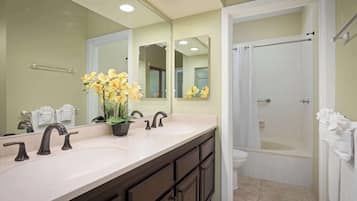A bathroom with a double sink vanity, a large mirror, a shower with a glass door, and a potted plant with yellow flowers.