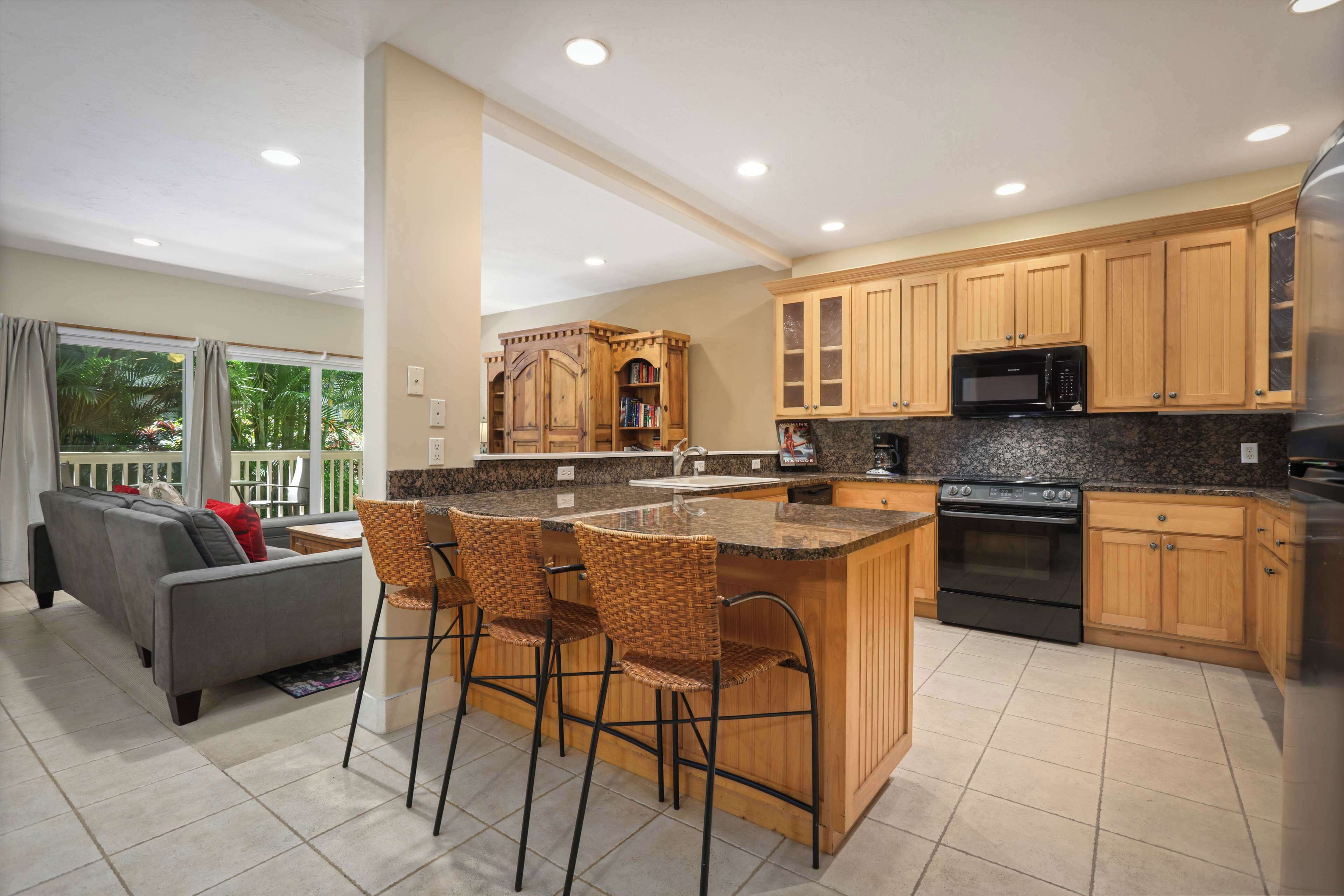 A modern kitchen with wooden cabinets, a granite countertop, a built-in oven, and a large island with bar stools.