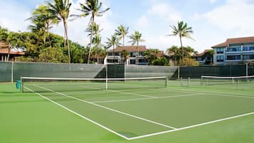 Een tennisbaan met een net, omringd door palmbomen en gebouwen.