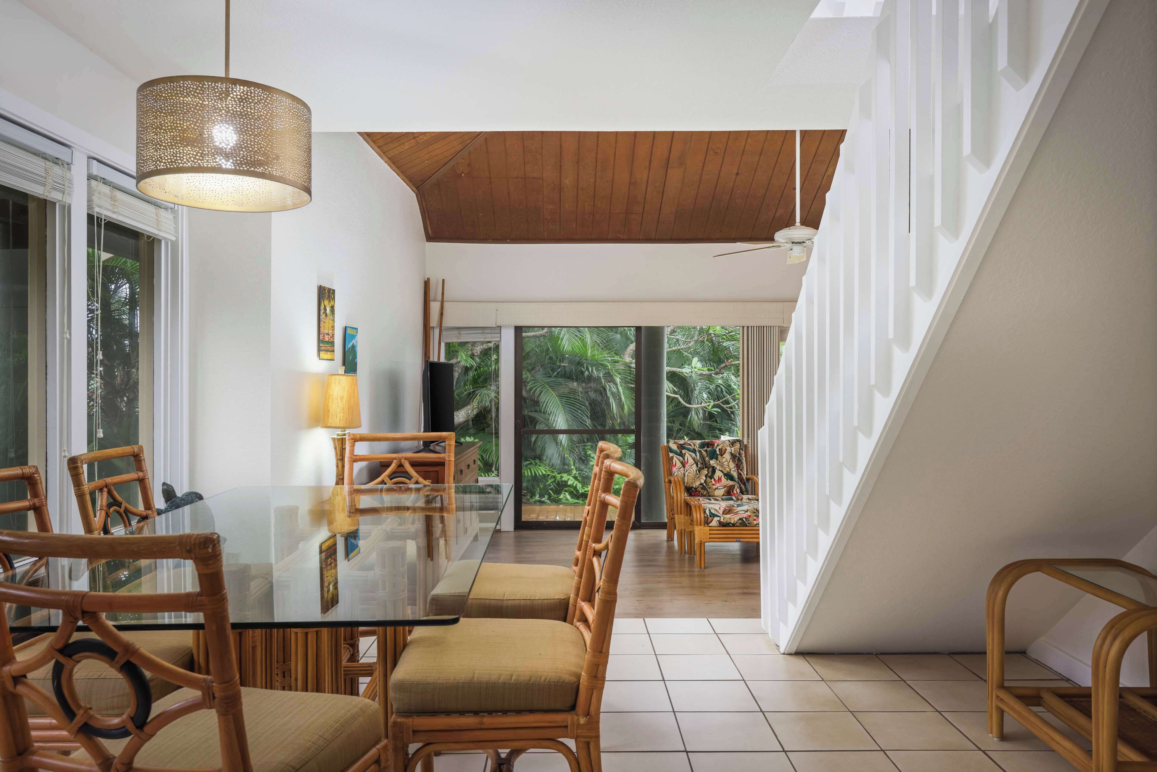 Un comedor moderno con mesa de vidrio, sillas de madera y una lámpara colgante.