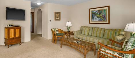 A living room with a sofa, armchairs, a coffee table, a television, and a ceiling fan.