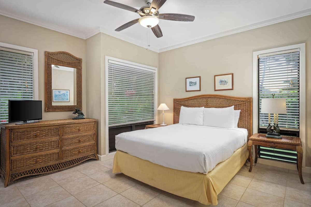 A hotel room with a bed, a television on a wooden dresser, and a ceiling fan.