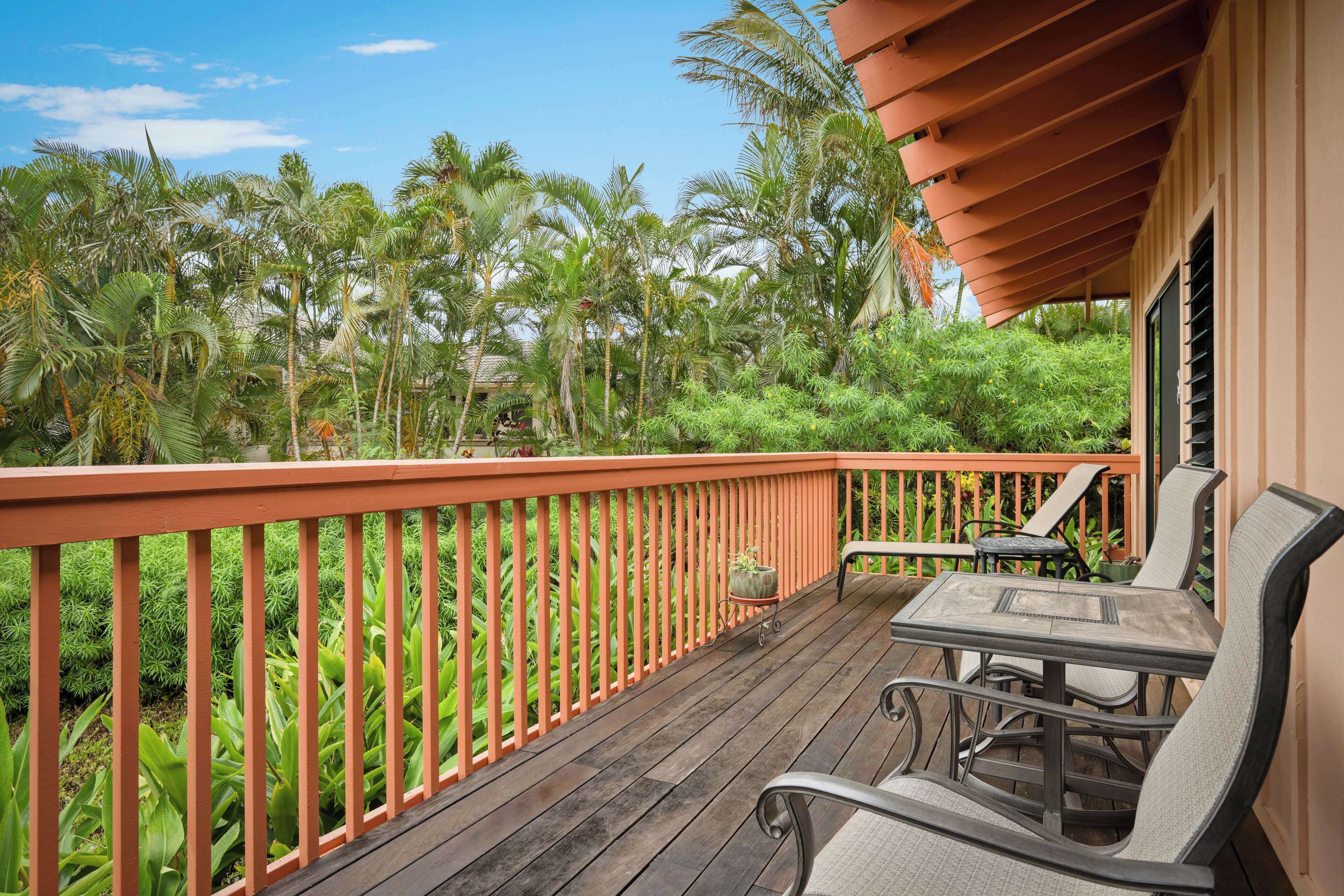 A wooden deck with a table and chairs, surrounded by lush greenery and palm trees.