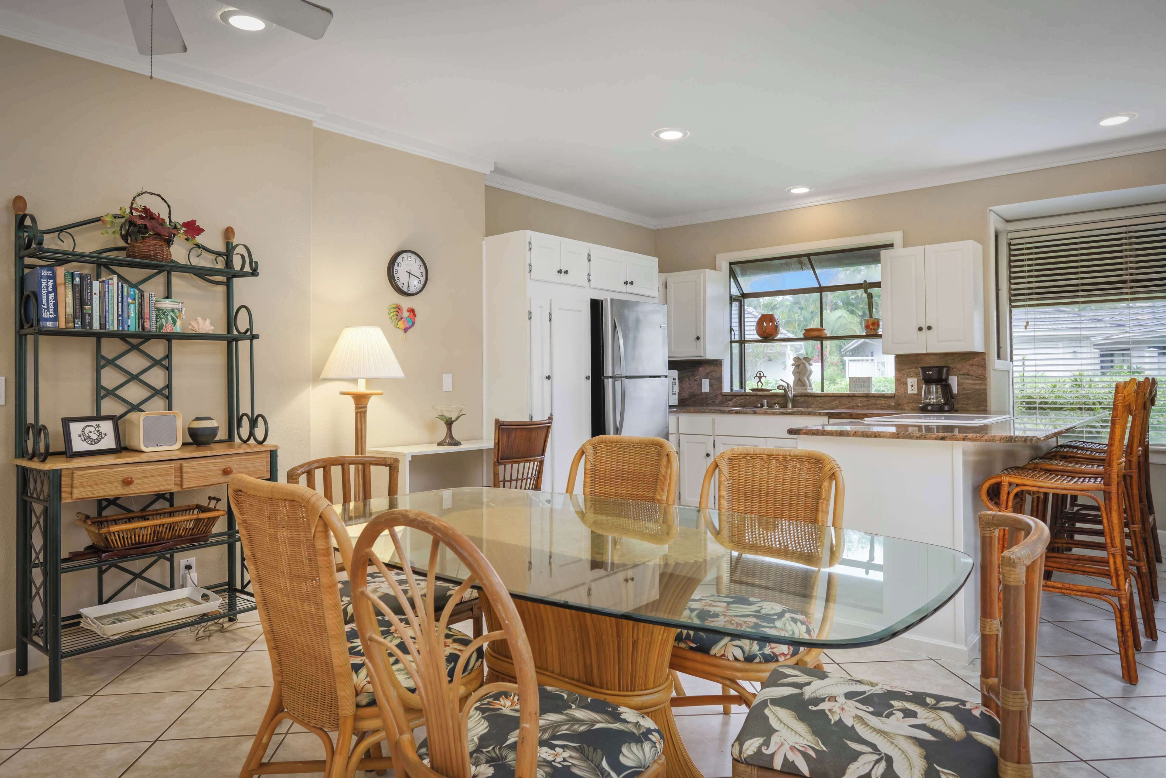 A modern kitchen with white cabinets, a stainless steel refrigerator, and a dining area with wicker chairs and a glass table.