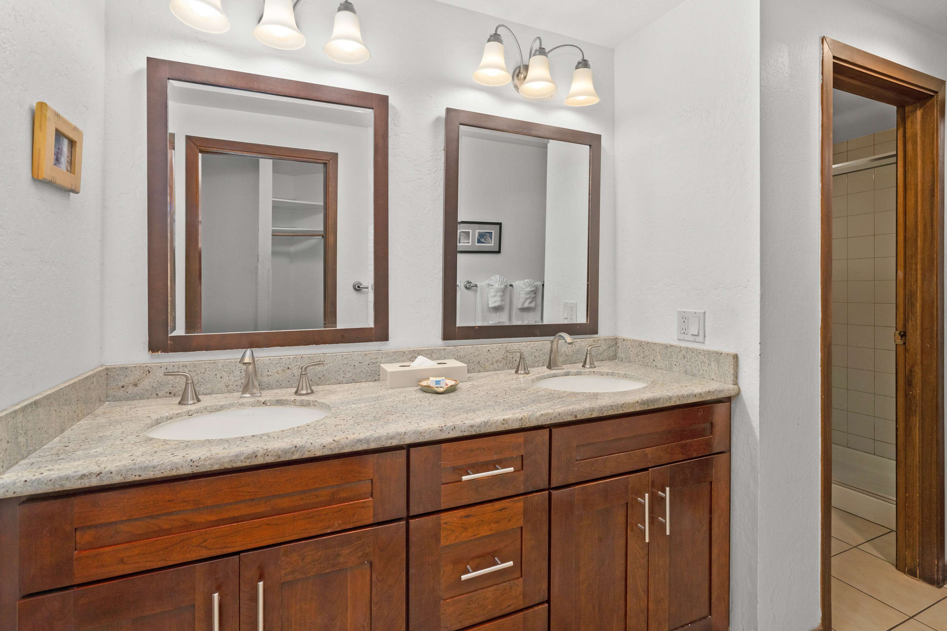 A bathroom with two sinks, wooden cabinets, and a large mirror with lights.