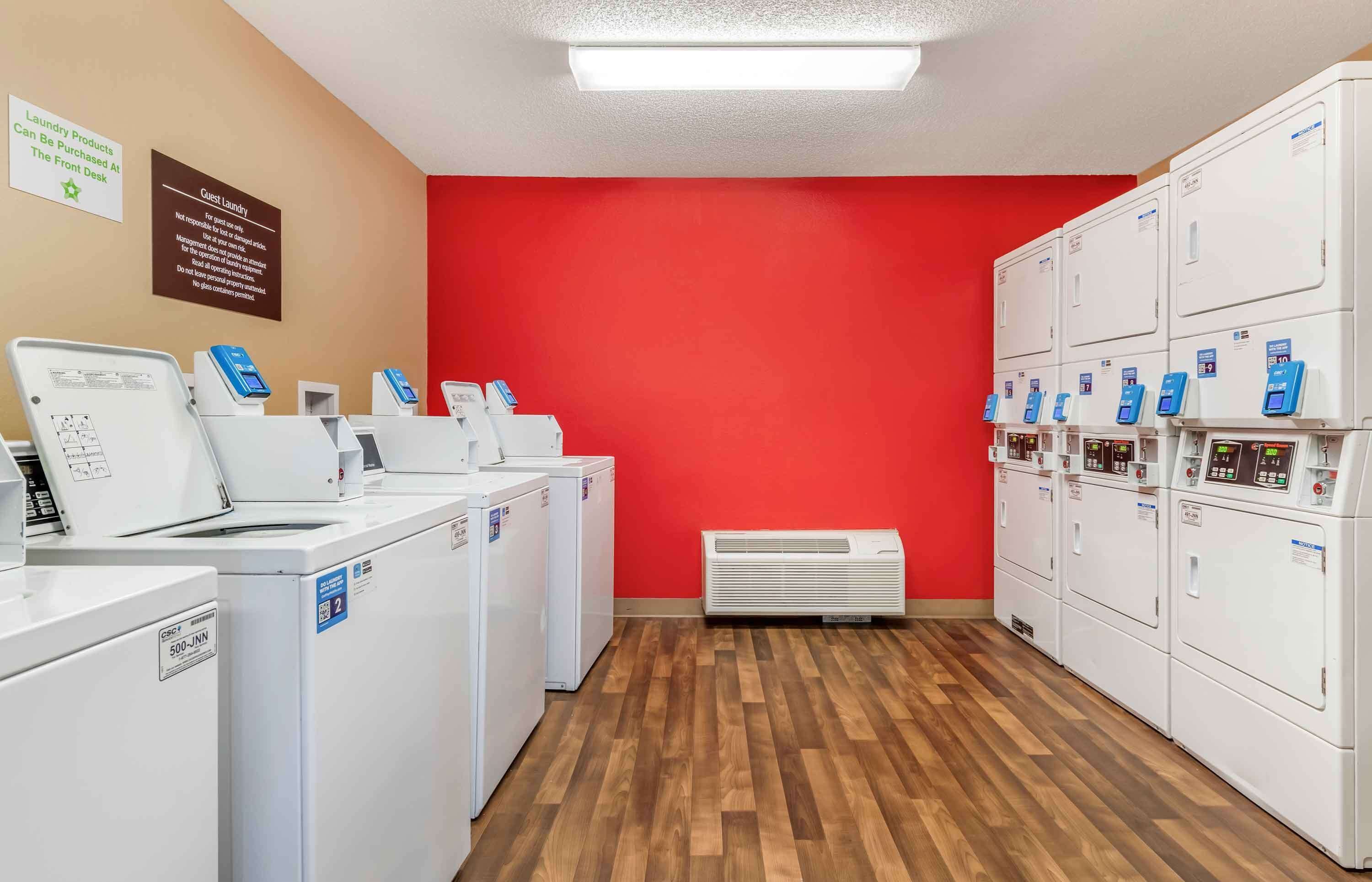 A laundry facility with multiple washing machines and dryers, a red wall, and a wooden floor.