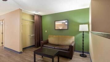 A hotel room with a brown leather sofa, a small table, a standing lamp, and a green accent wall.