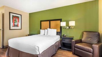 Een hotelkamer met een groot bed, een nachtkastje met een lamp, een stoel en een ingelijst schilderij aan de muur.