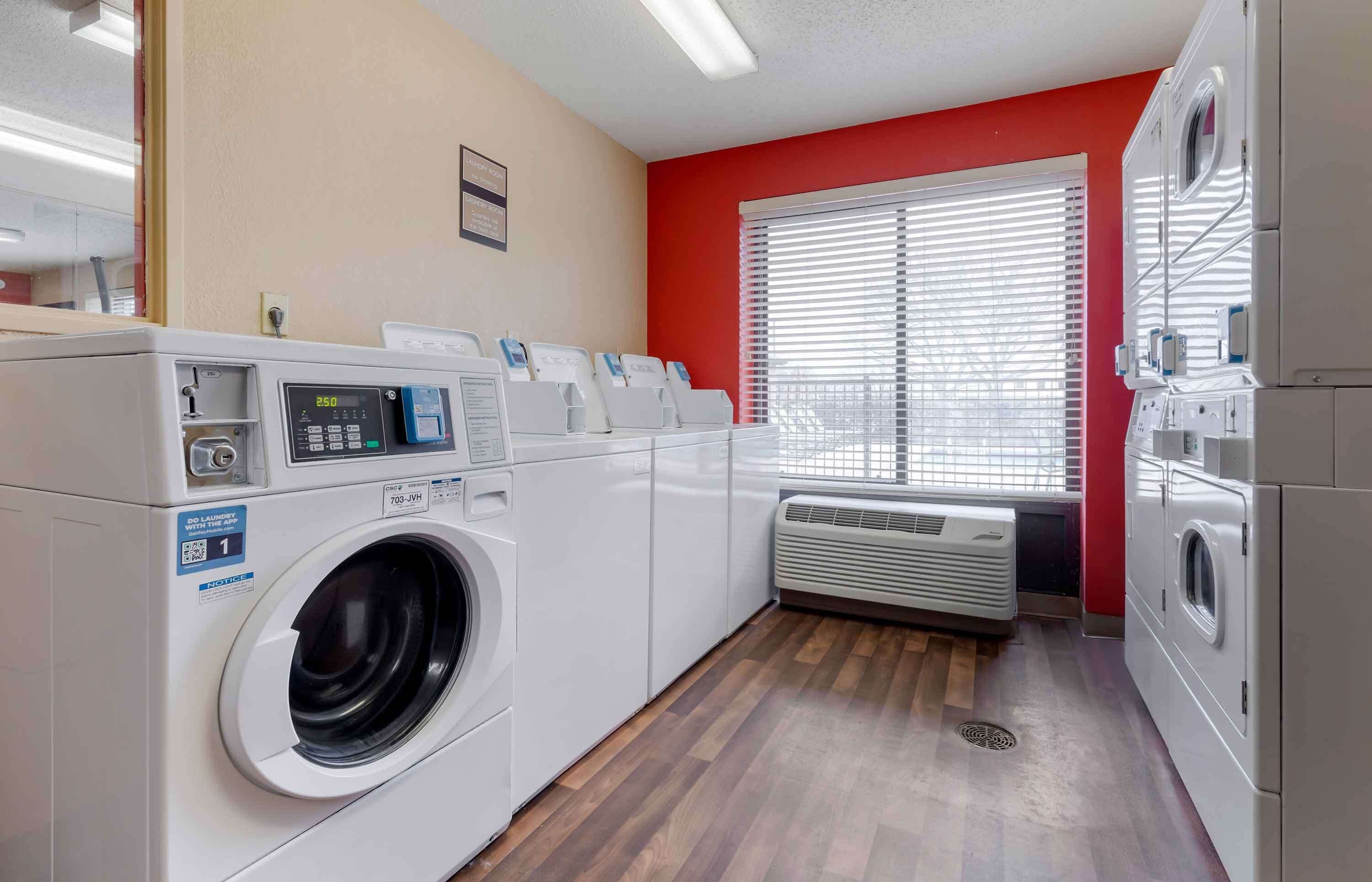 Une buanderie équipée de plusieurs machines à laver, d’un sèche-linge et d’une fenêtre à ventilation.