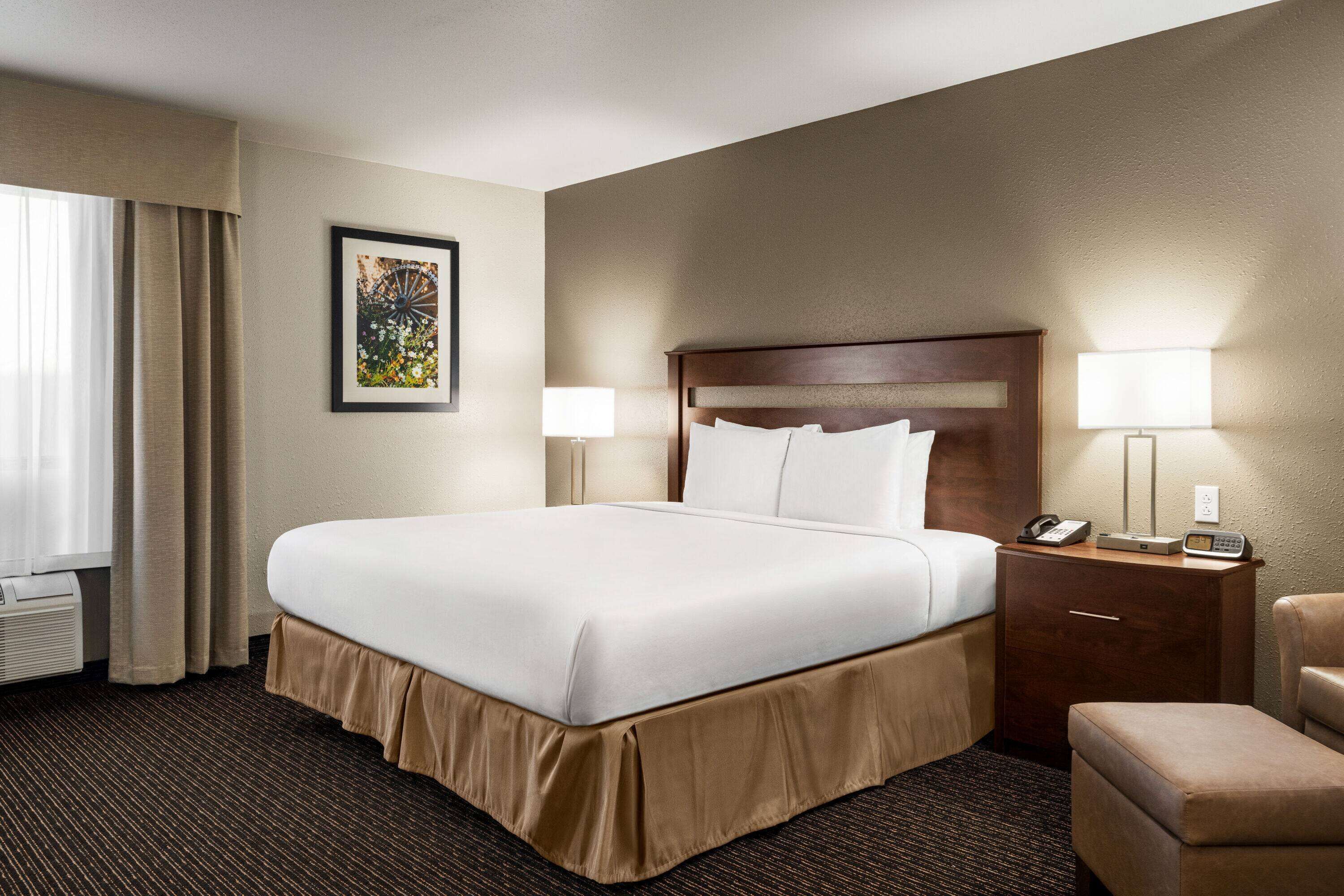 A hotel room with a large bed, two bedside lamps, a nightstand with a phone and a lamp, and a chair.