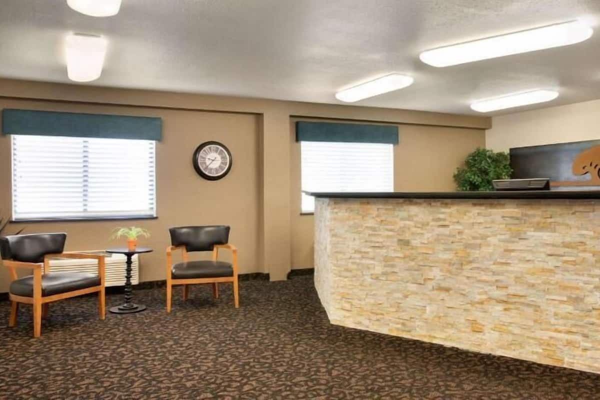 A reception area with a stone counter, two wooden chairs, a clock, and a potted plant.