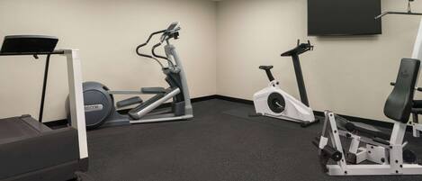 A gym with cardio equipment, a weight bench, and a TV screen on the wall.