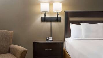 A hotel room with a bed, a nightstand with a phone, and a wall-mounted lamp.