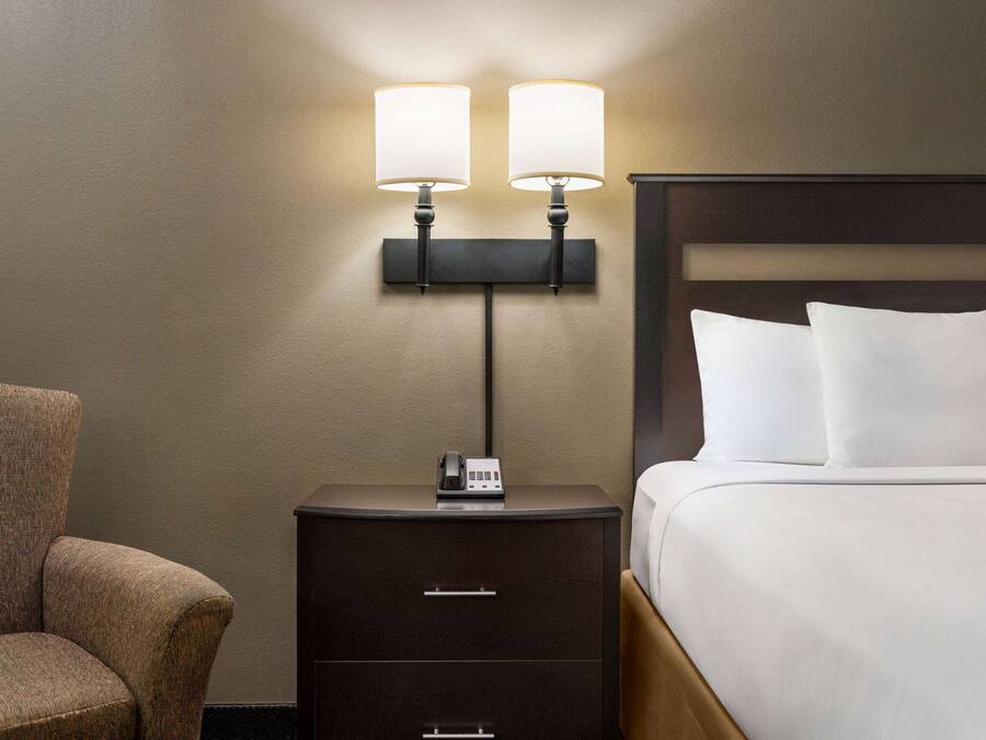 A hotel room with a bed, a nightstand with a phone, and a wall-mounted lamp.