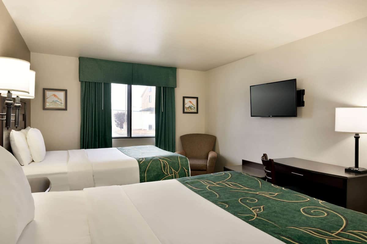 A hotel room with two beds, a desk, a chair, a TV, and a window with curtains.