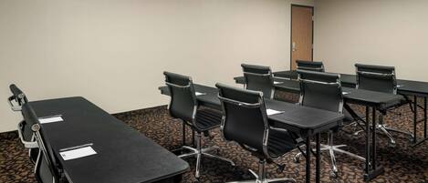 A conference room with six tables and chairs, carpeted floor, and a door in the background.