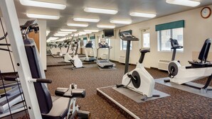 Un gimnasio con varias máquinas de ejercicio, un reloj en la pared y una ventana con persianas.