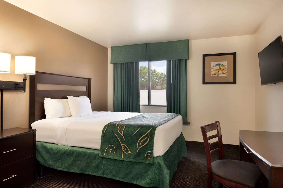 A hotel room with a bed, a desk, a chair, a TV, and a window with curtains.