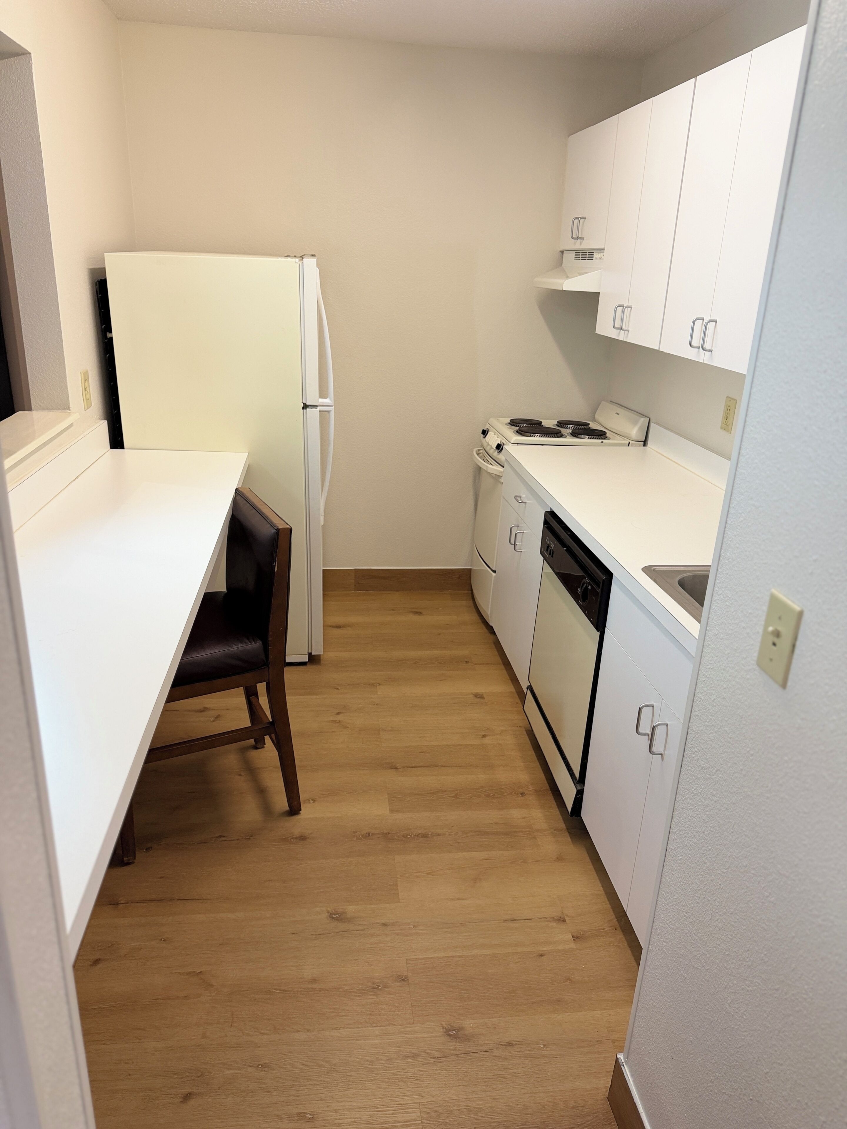 A compact kitchen with white cabinetry, a refrigerator, a stove, and a dishwasher.