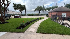 A parking lot with a paved walkway, green grass, and a brick building with a sign. - Extended Stay America Suites Houston Med Ctr NRG Park Kirby (Houston)