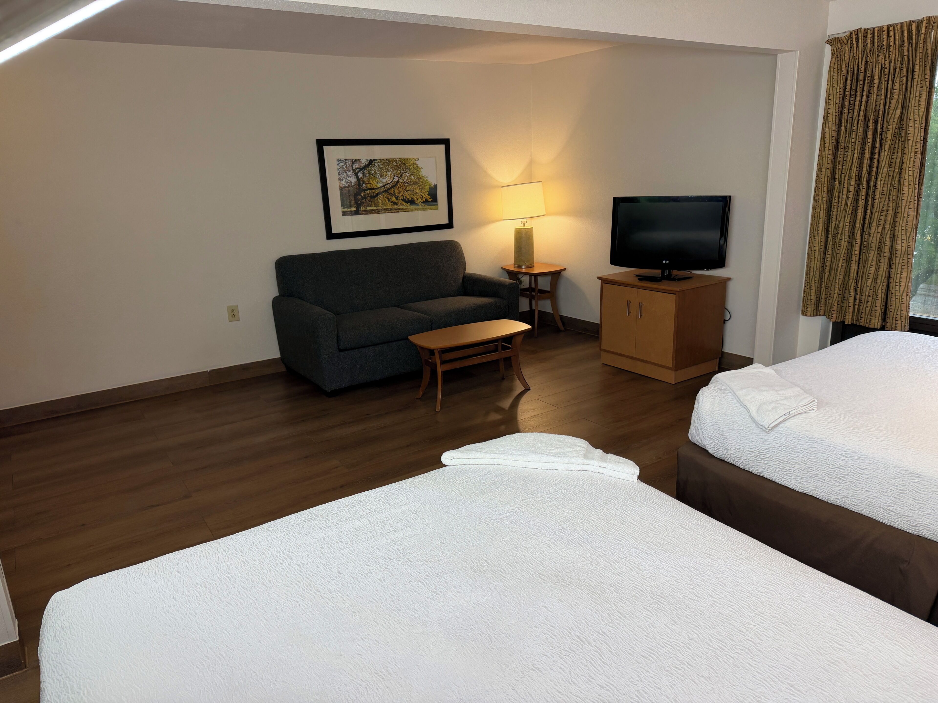 A hotel room with a sofa, a small table, a TV on a cabinet, and two beds.