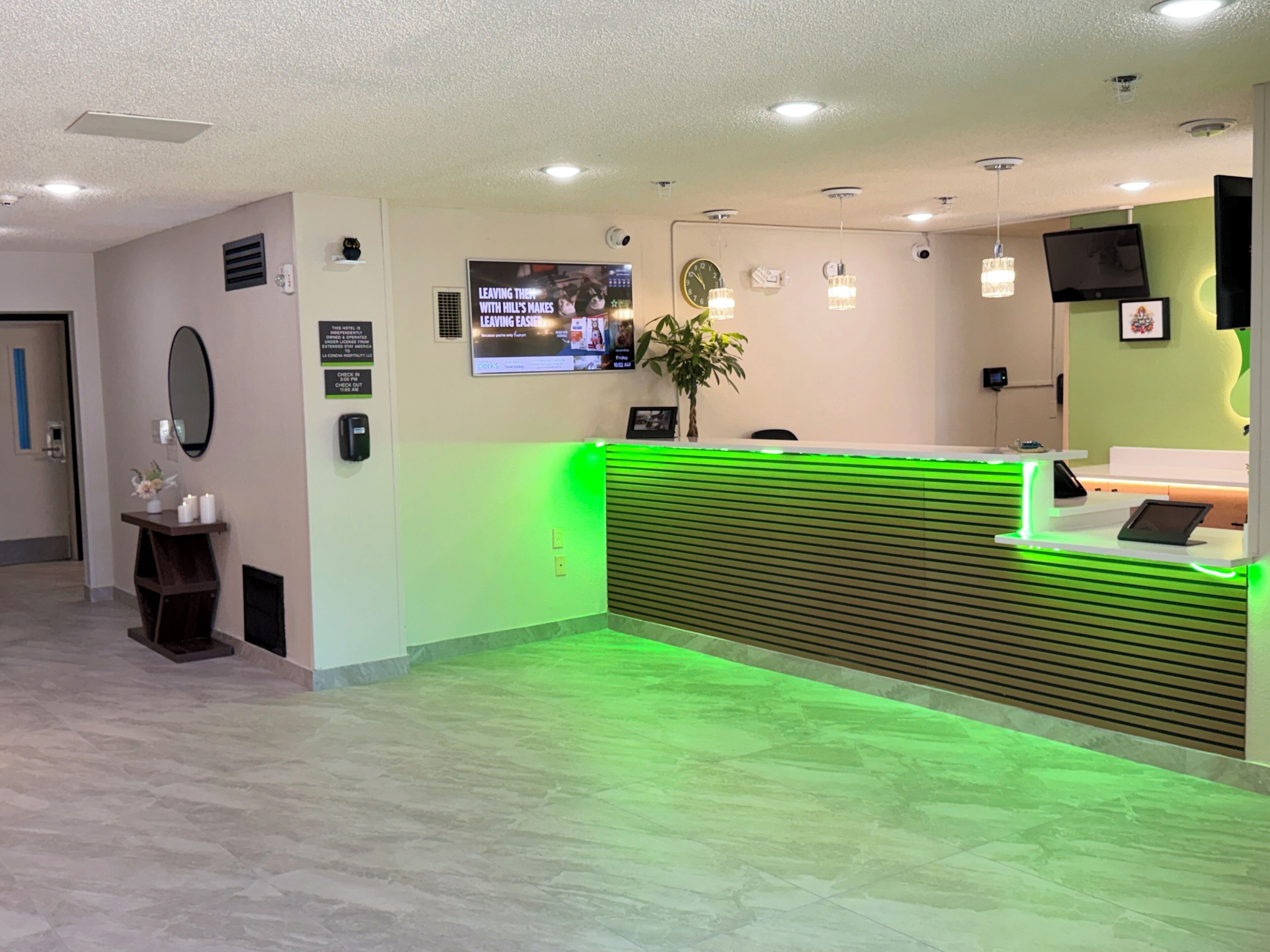 Un espace d’accueil avec un comptoir d’accueil éclairé en vert, une horloge et un écran de télévision.